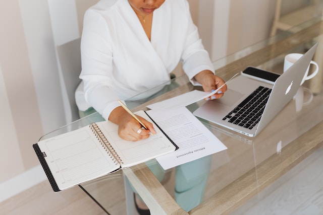 Person sitting at a glass-top table taking notes and looking over documents